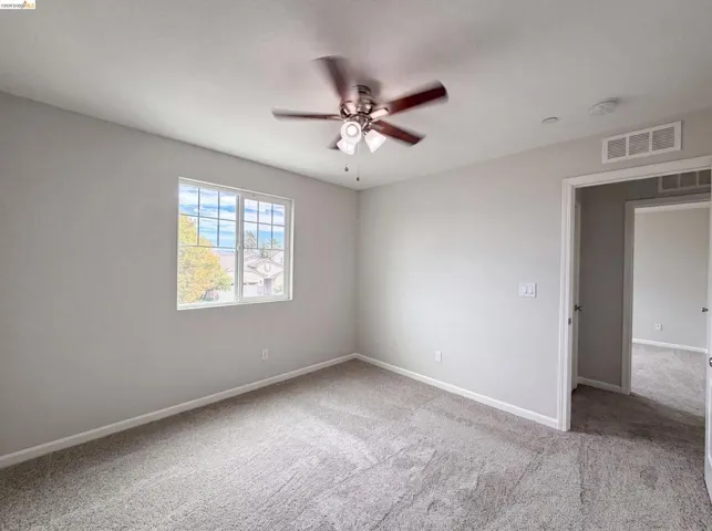 Carpeted interior space featuring a grid-paned window, a ceiling fan with integrated lighting, and neutral wall tones