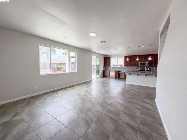 Open-concept living space featuring large format tile flooring, a kitchen with rich wood cabinetry, stainless steel appliances, a tiled backsplash, and recessed lighting