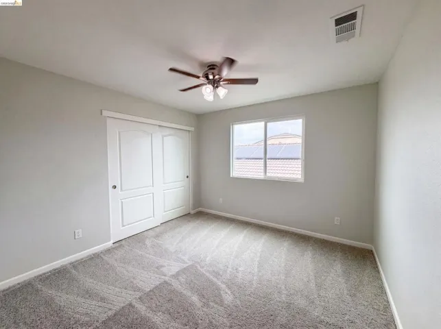 Carpeted room with a ceiling fan, a window, and sliding closet doors