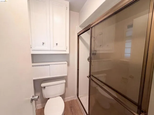 Bathroom featuring a walk-in shower with a framed glass enclosure, a white toilet, and wood-finish flooring