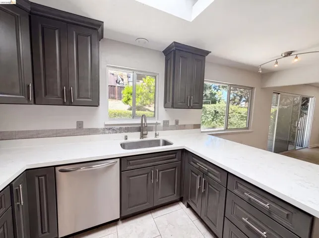 Kitchen featuring dark wood-finish cabinetry, light-toned countertops, and a stainless steel dishwasher