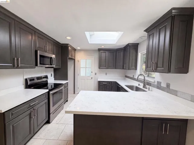 Kitchen featuring dark wood-finish cabinetry, light-toned countertops, stainless steel appliances, a skylight, and recessed lighting