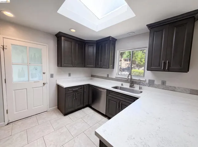 Kitchen featuring a skylight, dark wood-finish cabinetry, light-toned countertops, tile flooring, and a stainless steel sink with a gooseneck faucet