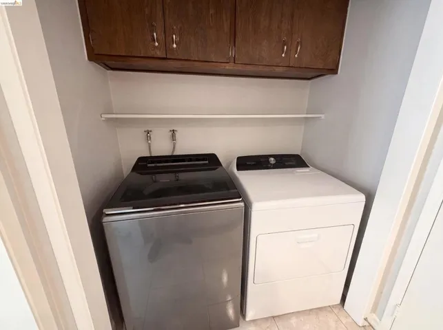 Dedicated laundry area featuring a white appliance set, overhead wood cabinetry, and a white storage shelf