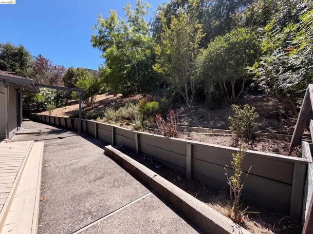 Outdoor concrete patio with wood-tone decking and a terraced hillside featuring retaining walls and mature trees