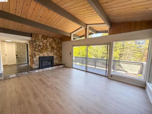 Vaulted wood-paneled ceilings with exposed beams, a stone fireplace, and light wood-finish flooring