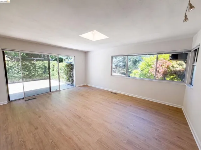 Spacious room featuring wood-finish flooring, a large sliding glass door with exterior access, multiple windows, a square ceiling light, and track lighting