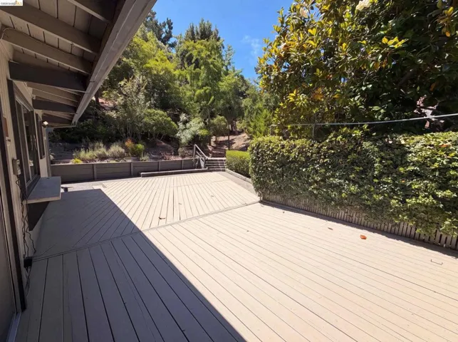 Spacious outdoor deck featuring light-toned composite decking, a built-in planter, and a mature privacy hedge