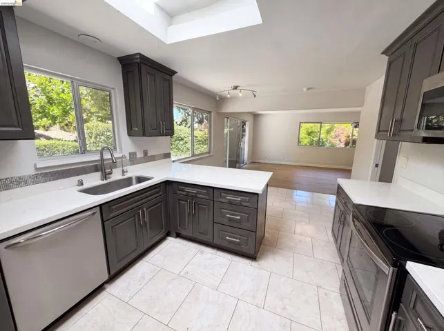 Kitchen featuring gray cabinetry, white countertops, stainless steel appliances, and a skylight