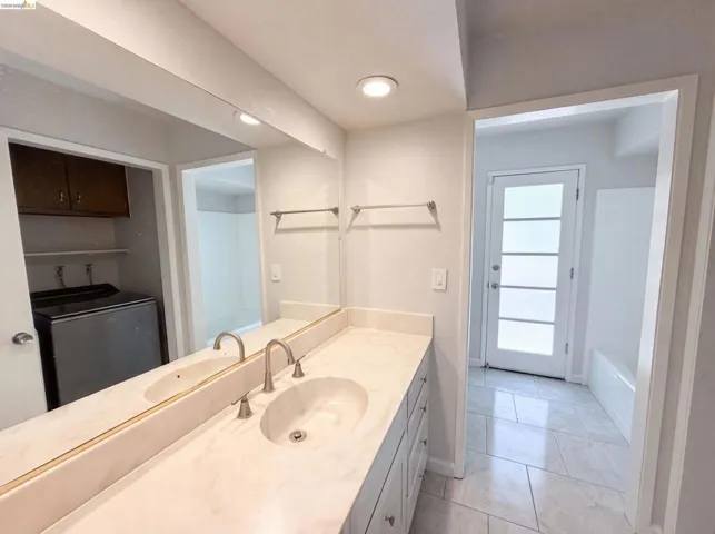 Dual vanity with integrated sinks, brushed nickel fixtures, a full-width wall mirror, and white cabinet storage