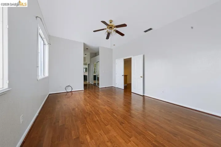 Spacious room featuring wood-finish flooring, vaulted ceiling, and dual windows