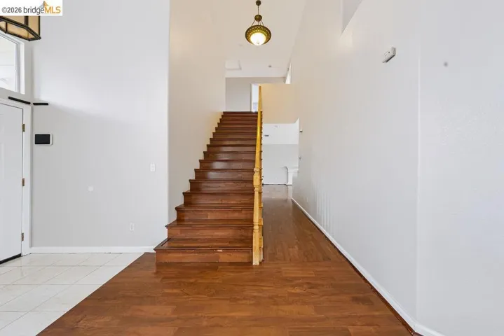 Grand entry foyer featuring hardwood stairs with a light wood banister, a dark wood-finish floor, and a contrasting tile entry