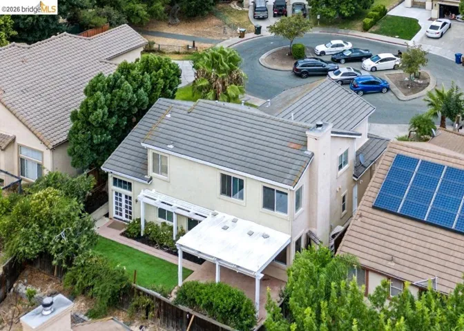 Expansive rear exterior featuring a covered patio, artificial turf lawn, and mature landscaping