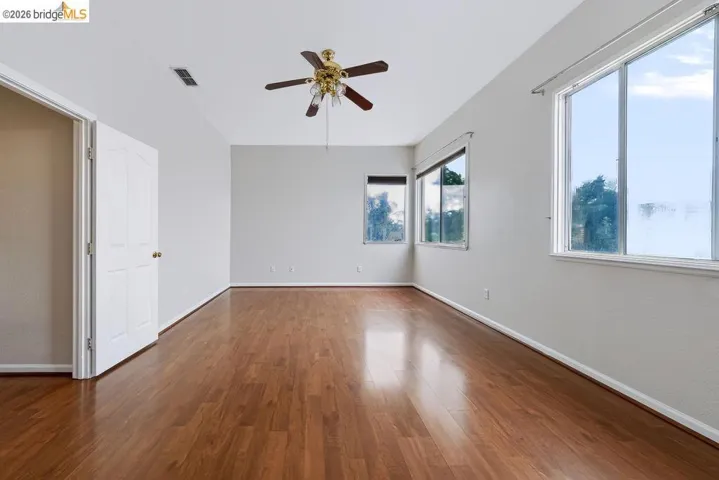 Spacious room featuring wood-finish flooring, a ceiling fan with light fixture, and multiple windows