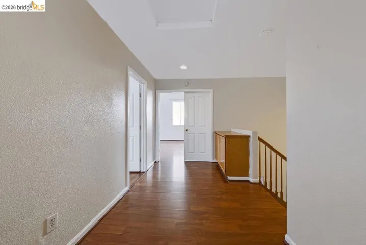 Hallway with wood-finish flooring, light tan walls, white trim, and a built-in wood-finish cabinet with a white top