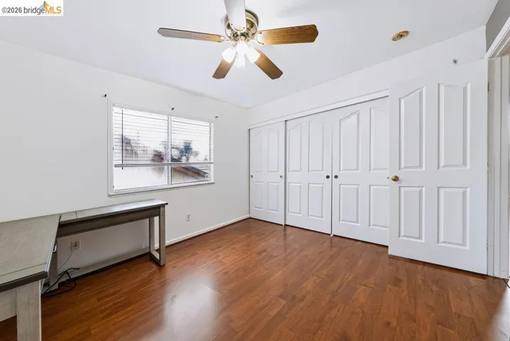 Bright room featuring rich wood-finish flooring, a ceiling fan with light fixture, and white bi-fold closet doors