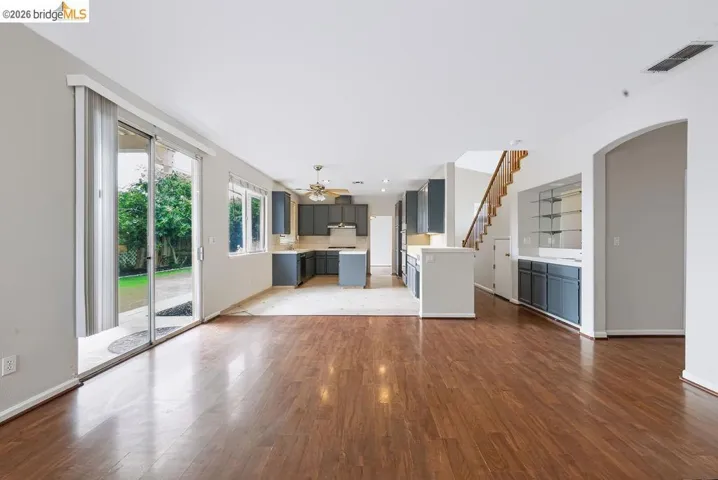 Expansive open-concept living area featuring wood-finish flooring, a contemporary kitchen with dark cabinetry, sliding glass doors to the exterior, multiple windows, and a built-in display cabinet with glass shelving