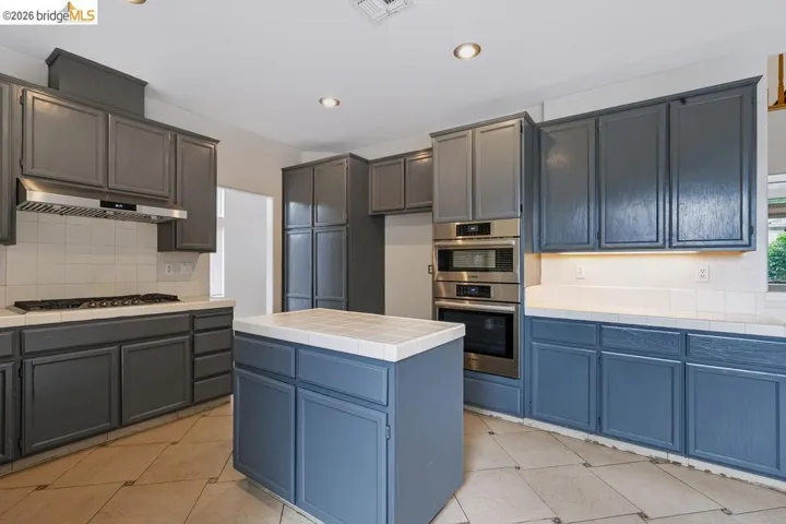 Kitchen featuring gray cabinetry, a central island with tiled countertop, and stainless steel built-in double ovens