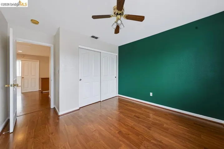 Bedroom featuring wood-finish flooring, a ceiling fan, a deep green accent wall, and double sliding closet doors