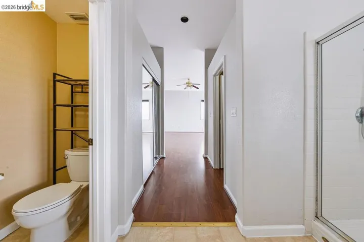 Hallway with wood-finish flooring, leading to a room with a ceiling fan