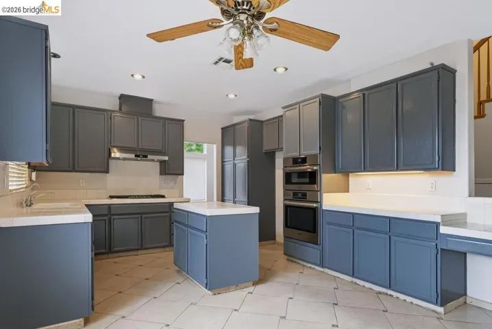 Spacious kitchen featuring extensive blue-gray cabinetry, a central island, recessed lighting, and a ceiling fan
