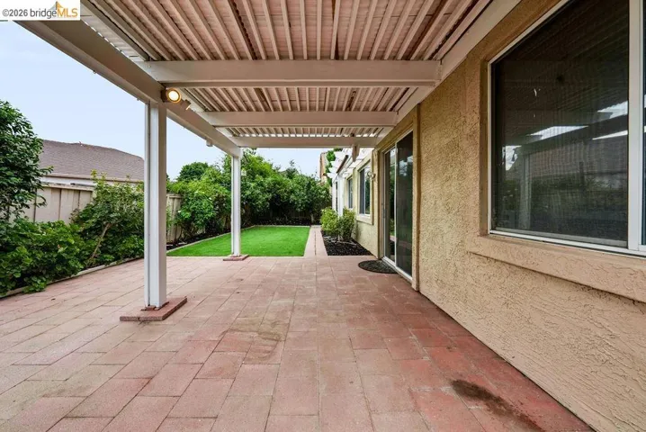 Expansive patio featuring red paver flooring and a white slatted pergola