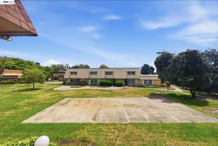 Expansive green space featuring mature trees and a large concrete pad
