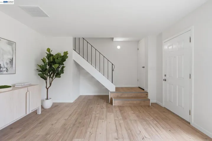 Entryway featuring wood-finish flooring, a white paneled entry door, and a staircase with a black wrought iron railing
