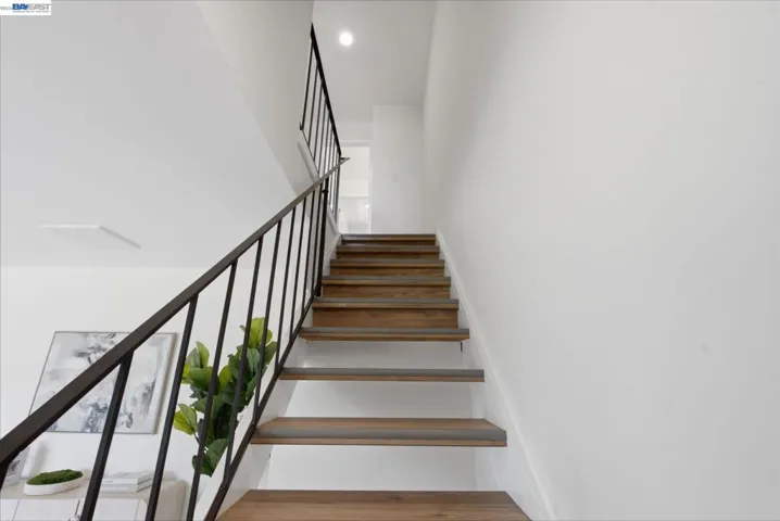 Floating staircase with wood-finish treads, white risers, and a black wrought iron railing
