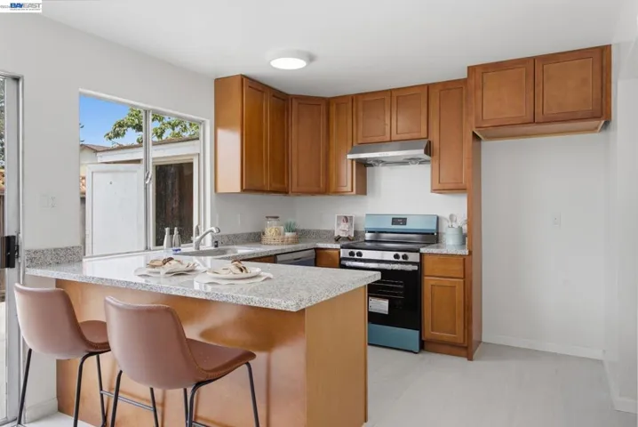 Kitchen featuring a peninsula with seating, light wood-finish cabinetry, light-toned countertops, and a modern range with a coordinating hood