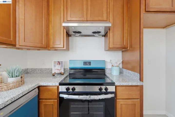 Kitchen featuring light wood-finish cabinetry, speckled countertops, stainless steel range hood, and a black and stainless steel range