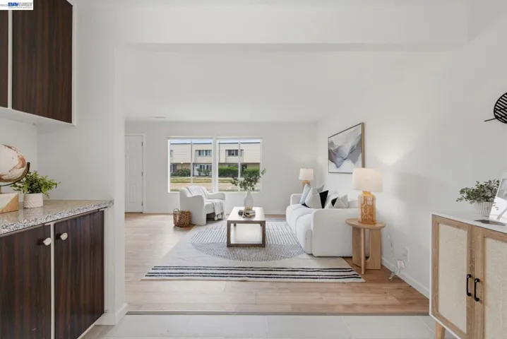 Spacious living area featuring light wood-finish flooring, white walls, and a large window offering natural light
