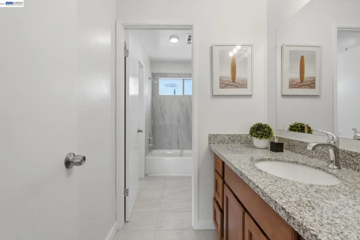 Bathroom featuring a light-toned granite countertop, a wood-finish vanity with cabinet storage, a chrome faucet, and a large mirror