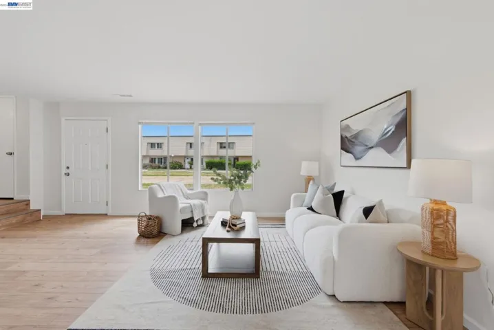 Open-concept living space featuring wood-finish flooring, white walls, and a large front window