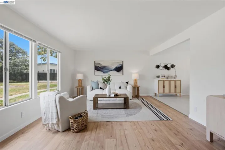 Bright living area featuring wood-finish flooring, white walls, and abundant natural light from multiple large windows