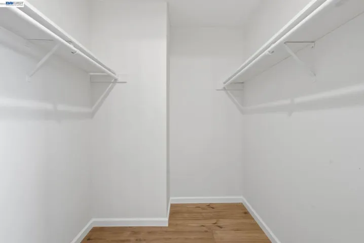 Built-in closet system featuring dual shelving and clothing rods, white walls, white baseboards, and wood-finish flooring