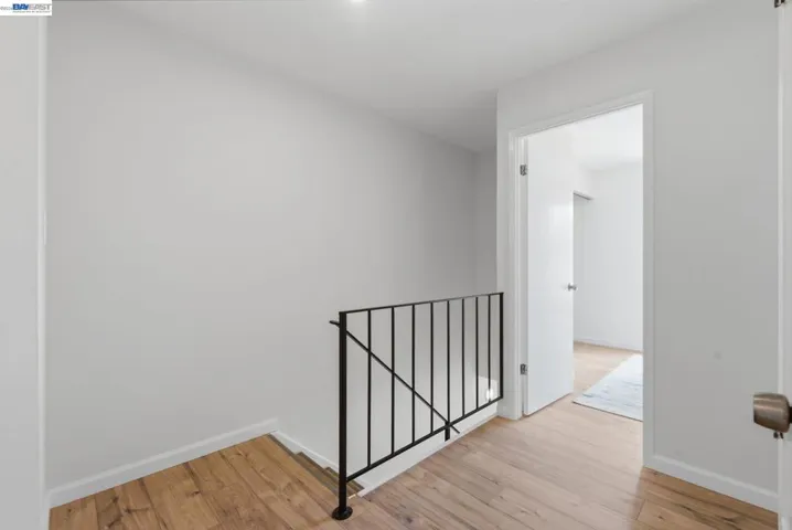 Hallway featuring wood-finish flooring and a black metal stair railing