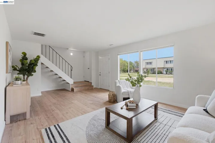 Spacious living area featuring wood-finish flooring, white walls, and bright window light
