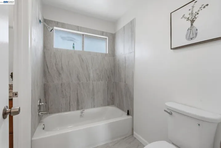 Bathroom featuring a white bathtub, light-toned tile surround, and a frosted window