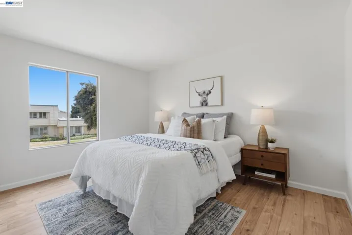 Bright bedroom featuring a large window, wood-finish flooring, white walls, and white baseboards