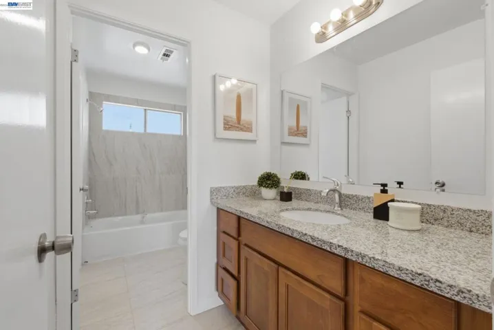 Bathroom featuring a wood-finish vanity with a speckled countertop, an integrated sink with a chrome faucet, and a wall-mounted light fixture