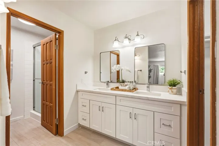 Fully updated bathroom with a dual-sink quartz vanity, rain shower with custom niche, private water closet, and walk-in closet