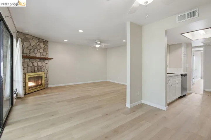 Spacious living area featuring wood-finish flooring, a stone fireplace with wood mantel, and overhead recessed lighting
