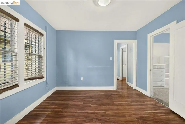 Spacious room featuring wood-finish flooring and two large windows with blinds