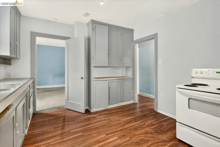 Kitchen featuring wood-finish flooring, light gray cabinetry, white countertops, and a built-in wall cabinet with open shelving