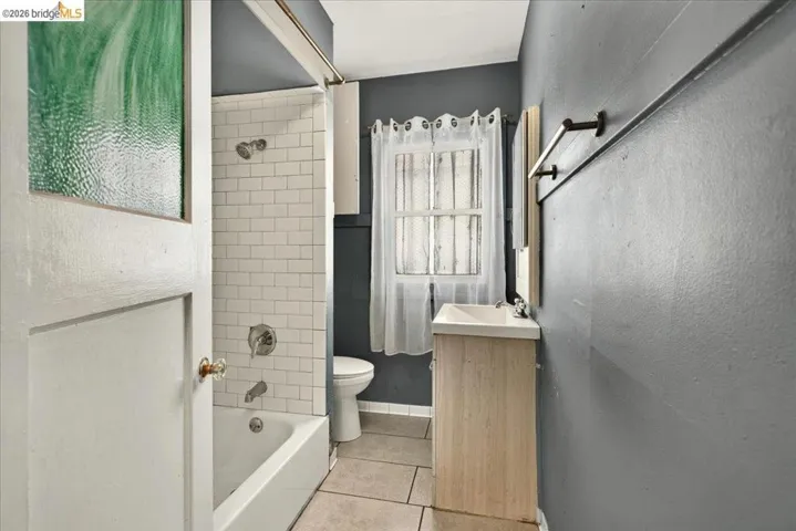 Bathroom featuring a white bathtub with subway tile surround, neutral-toned floor tiling, a single-pane window, and a vanity with a sink