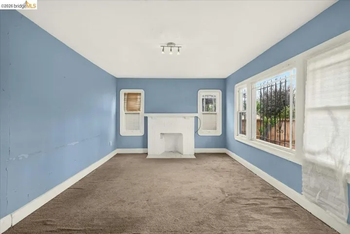 Spacious room featuring a white fireplace mantel, multiple windows with white trim, a track lighting fixture, and brown carpeting
