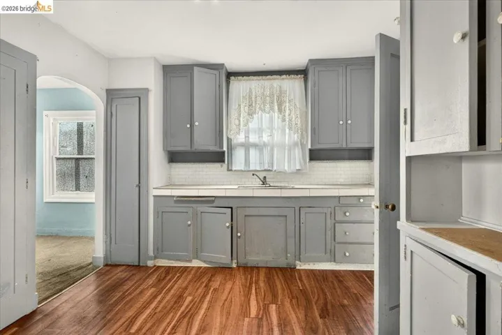 Kitchen featuring wood-finish flooring, gray cabinetry, white tile backsplash, and a window above the sink