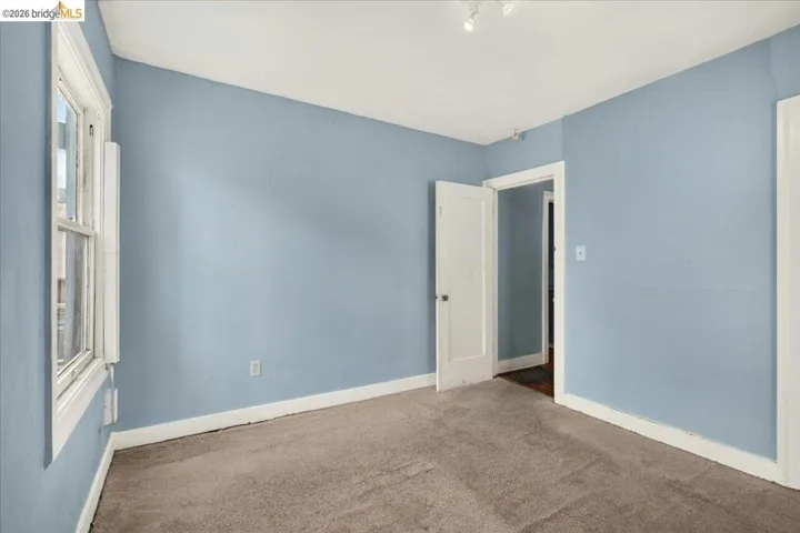 Room featuring a window, light blue painted walls, white trim, and neutral carpet flooring