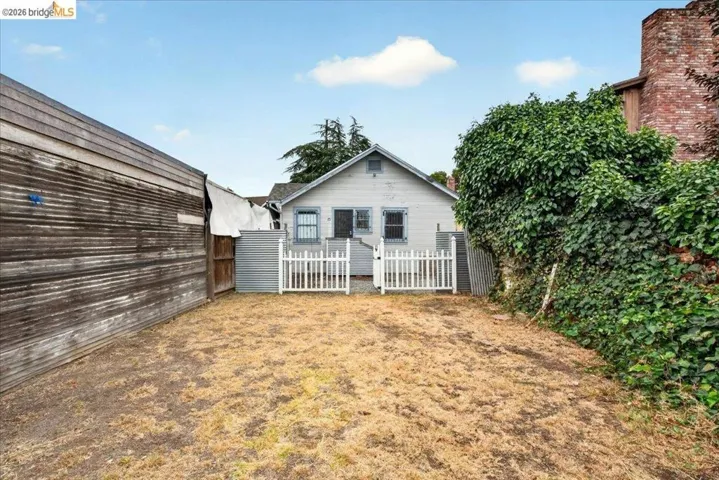 Cottage-style residence featuring a white picket fence, gray exterior siding, and multiple windows with dark shutters
